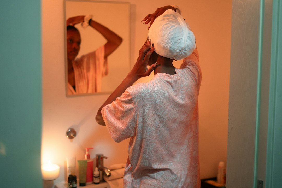 Woman applying towel to hair in bathroom mirror